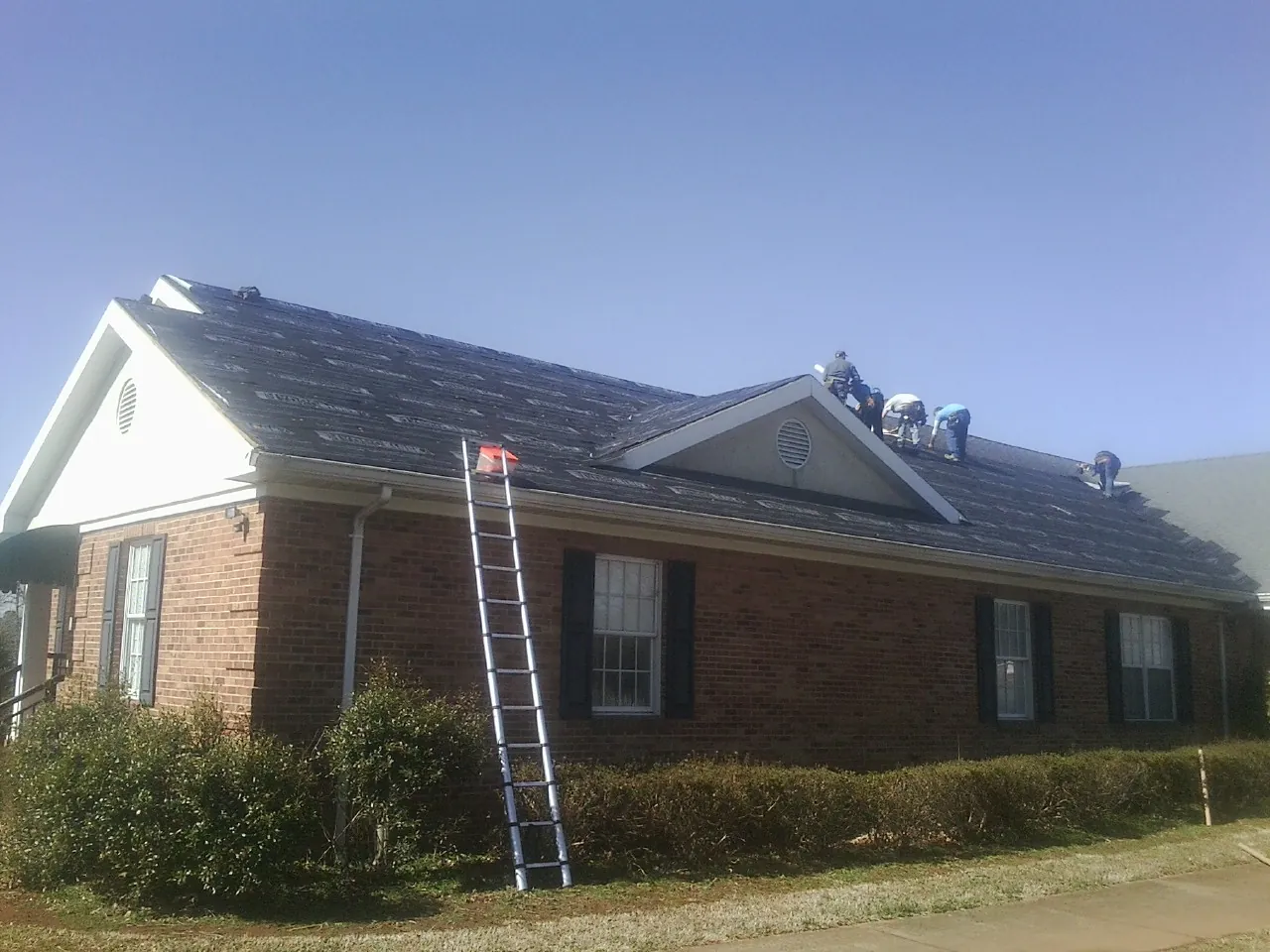 Crew tearing shingles off a brick ranch roof with a ladder set — Metal Roof Repair work by our crew in Coalville