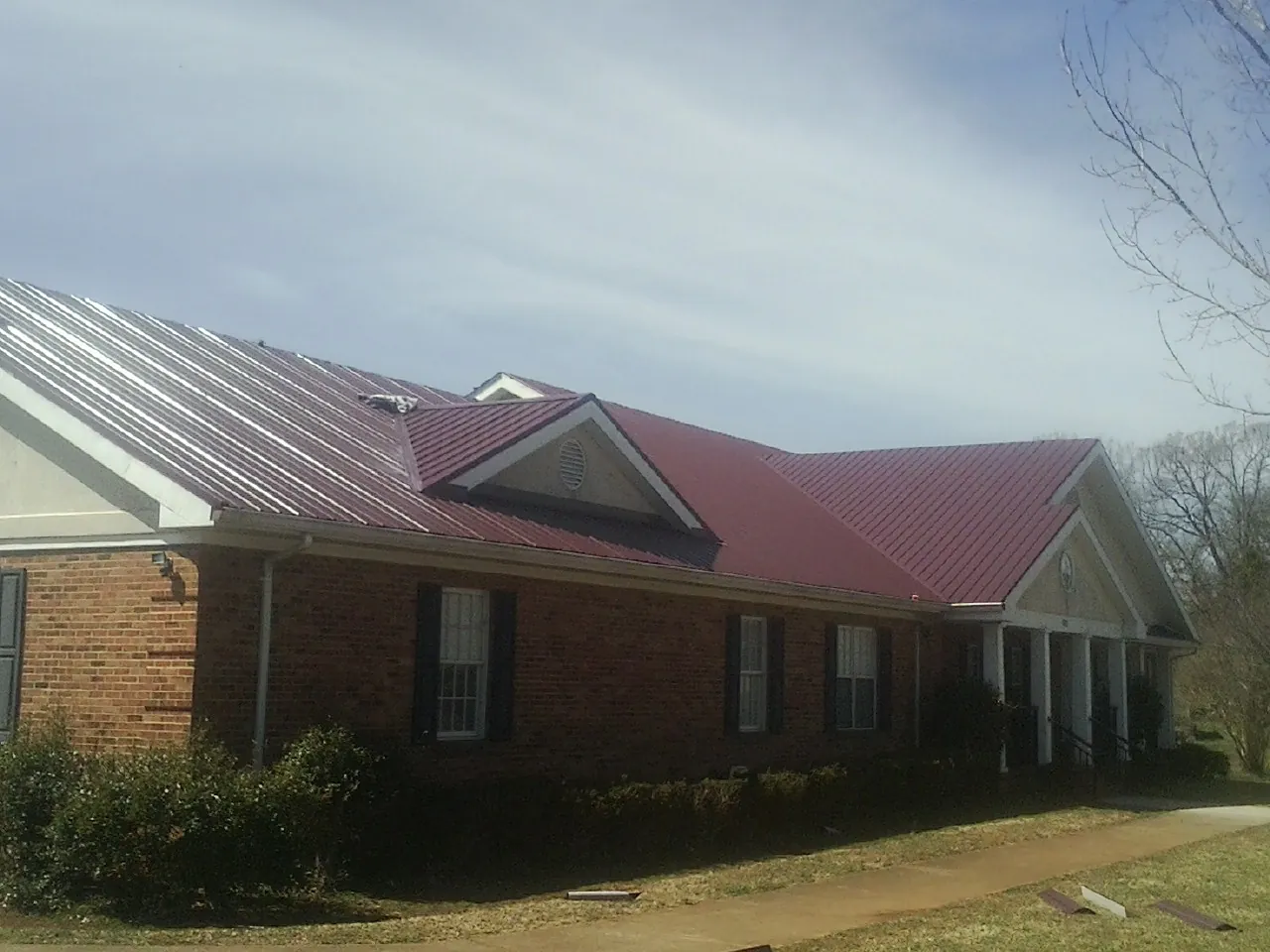 Red metal roof with gabled entries on a long brick building, from a Hail Damage Roof Repair job in Coalville