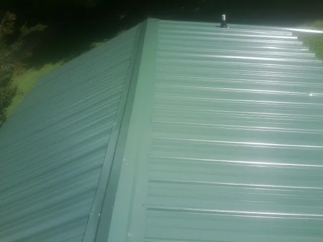 New green metal panels meeting at the ridge of a roof — Flat Roof Repair work by our crew in Coalville