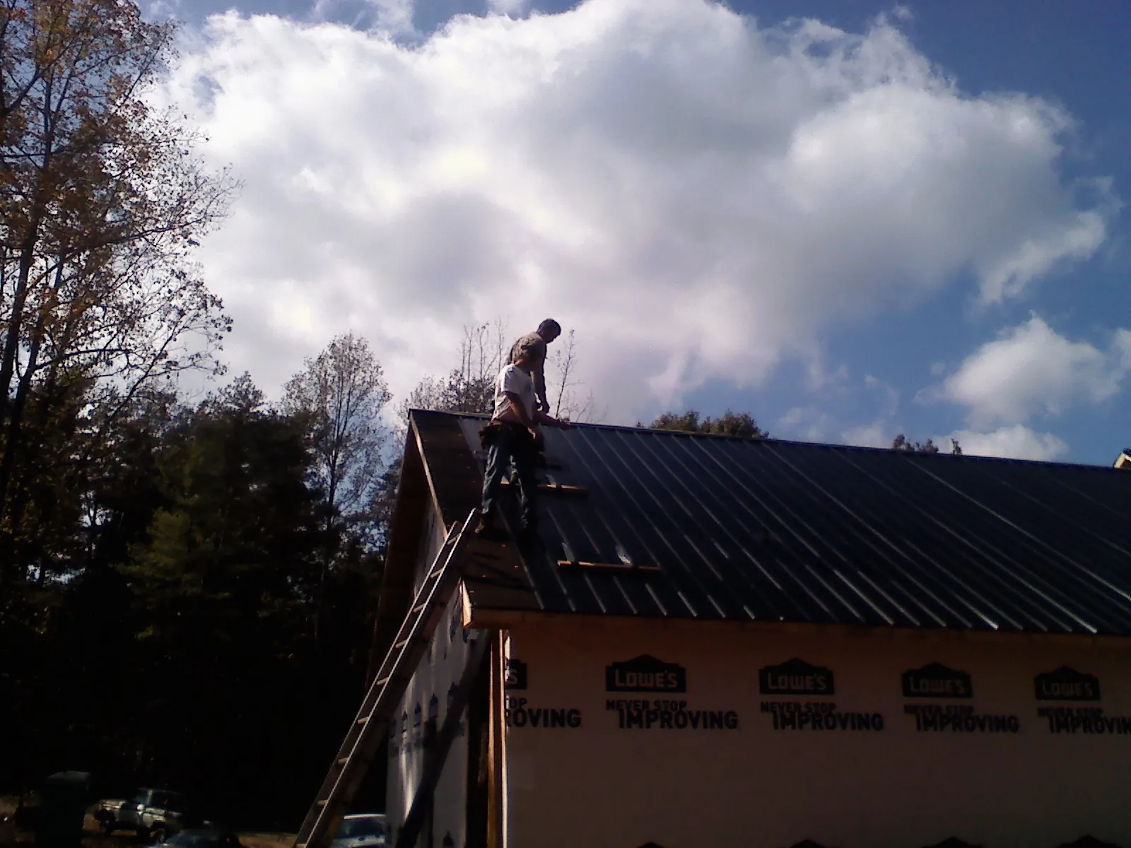 Roofer fastening dark metal panels high against a cloudy sky, from a Roof Inspection job in Coalville