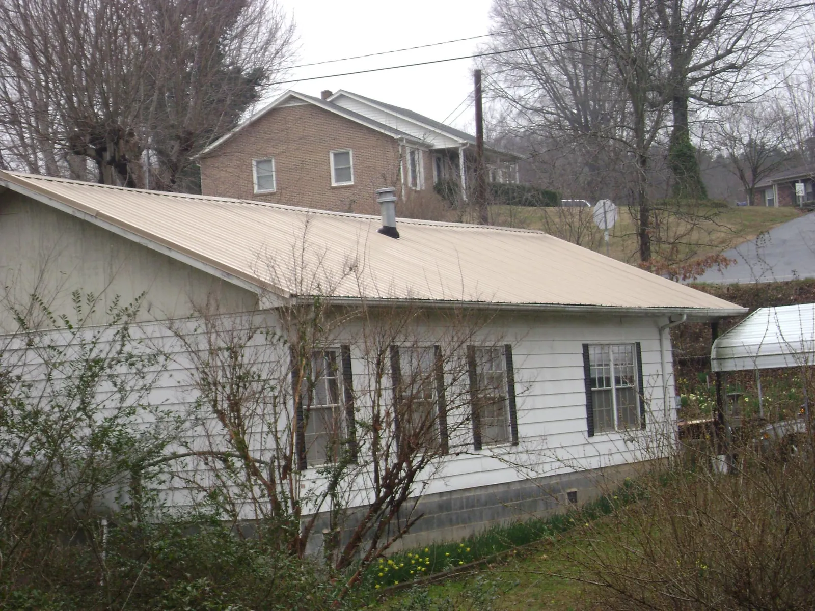 Tan metal roof on a white sided house set into a hillside — Commercial Roofing by Roofing Brothers in Coalville