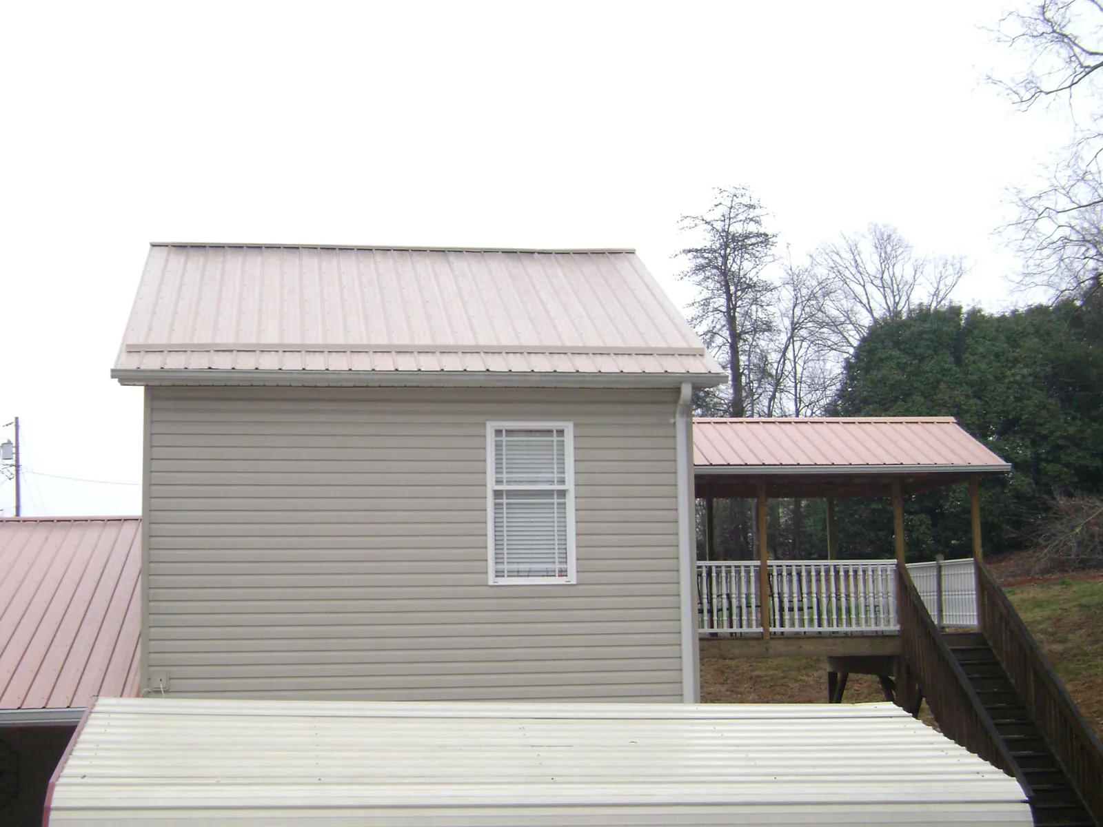 Tan metal roofs on a two story addition and attached porch, from a Roof Replacement job in Coalville